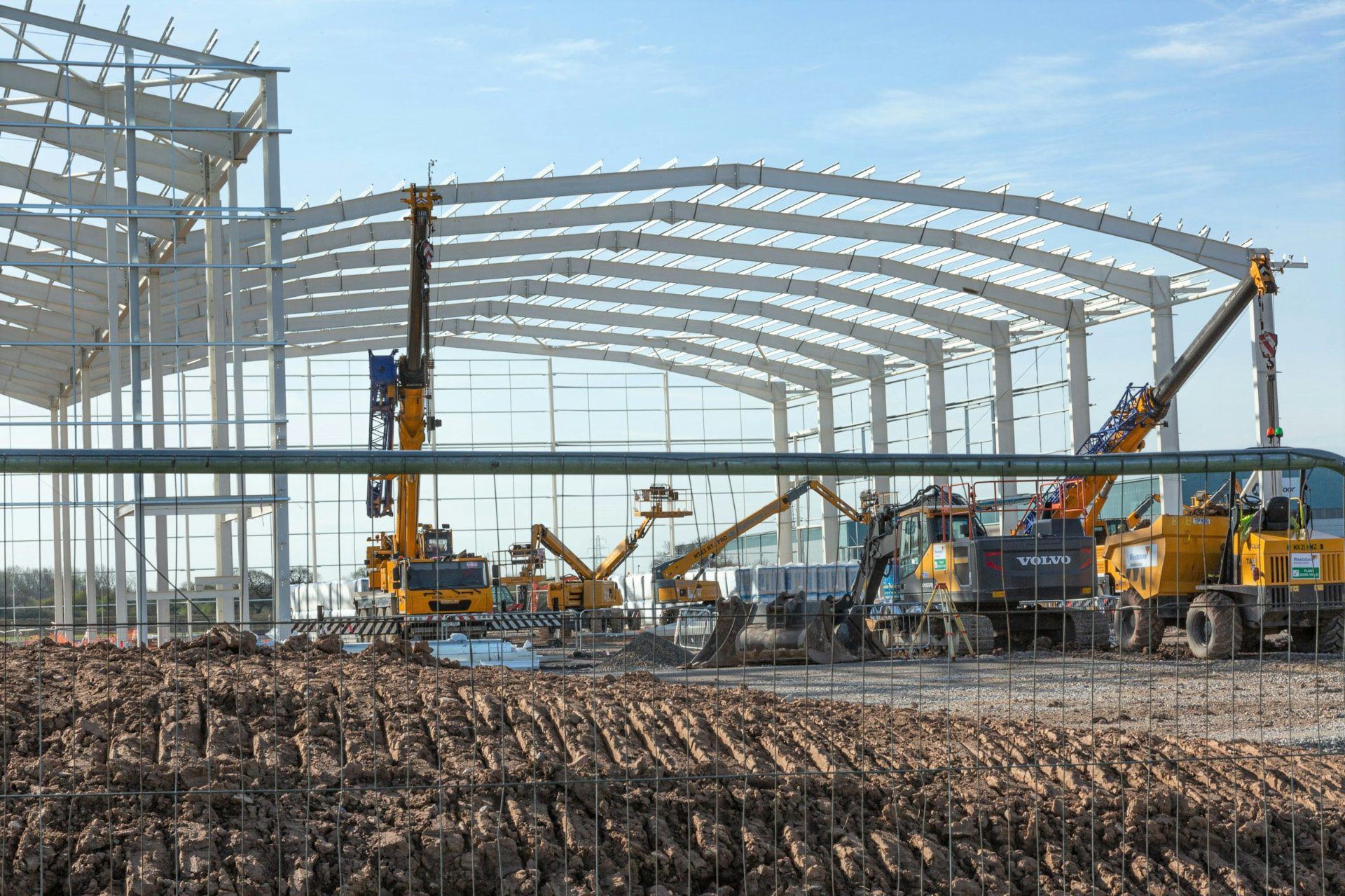 Steel-framed industrial building under construction with cranes and site equipment